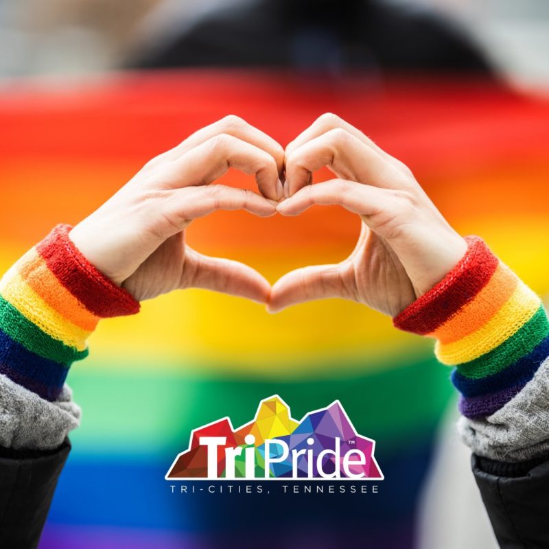 heart hands in front of a rainbow flag with TriPride logo