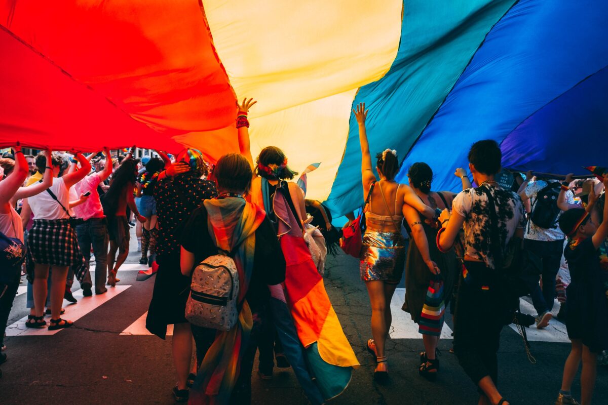 People under rainbow flag at a pride parade