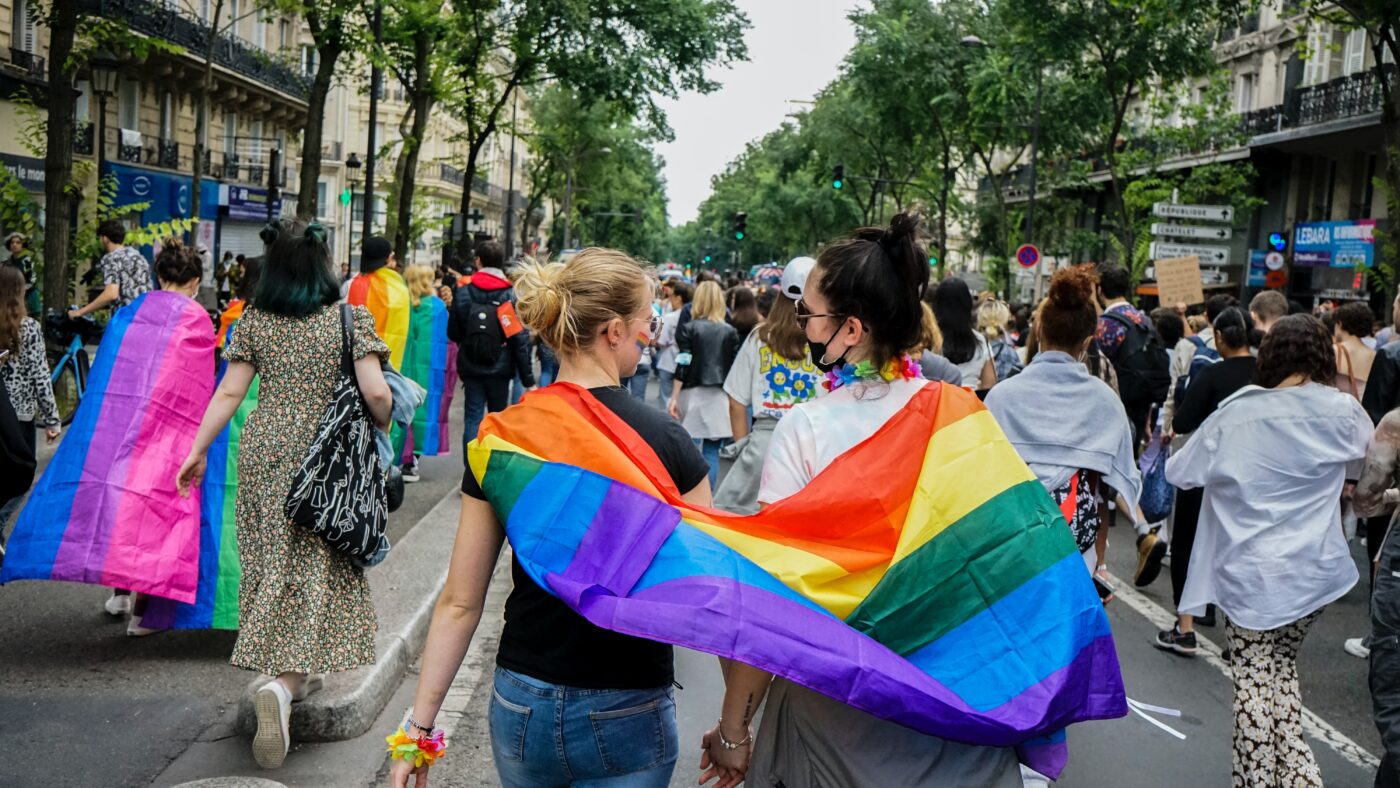 `Two people attending a pride festival with a rainbow flag wrapped around them
